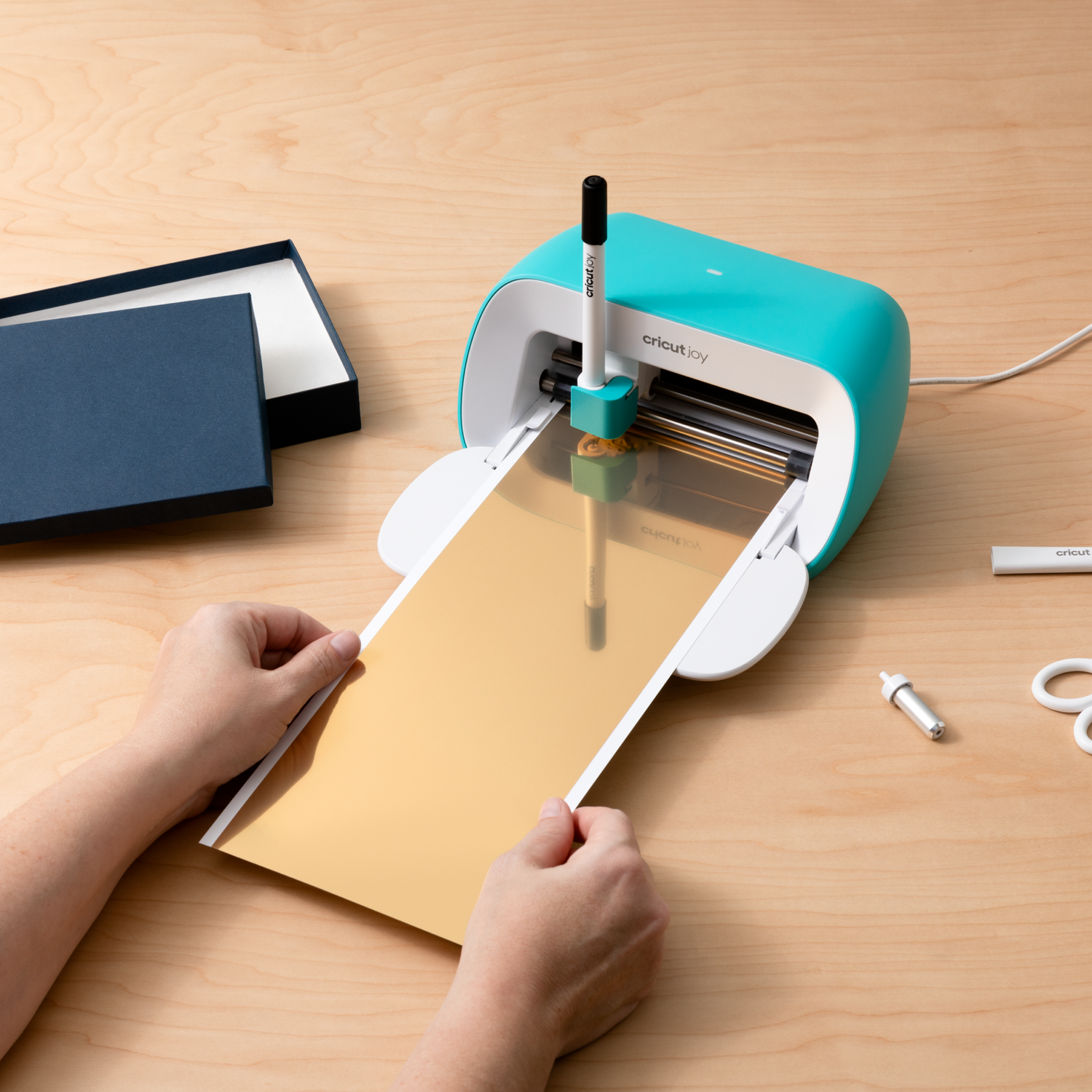 Cricut Joy cutting machine with gold paper and hands.