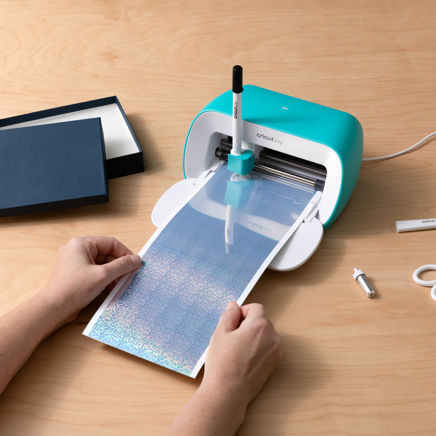 A crafting machine with a paper being inserted by hands. A box is in the background.