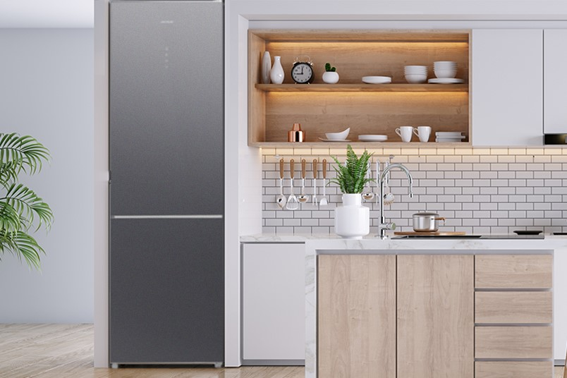 Un refrigerador moderno y gris en una cocina. Tiene una puerta degradada y está cerca de una estantería de madera.