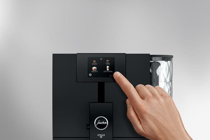 Mano tocando la pantalla de una cafetera Jura Ena 8 negra.