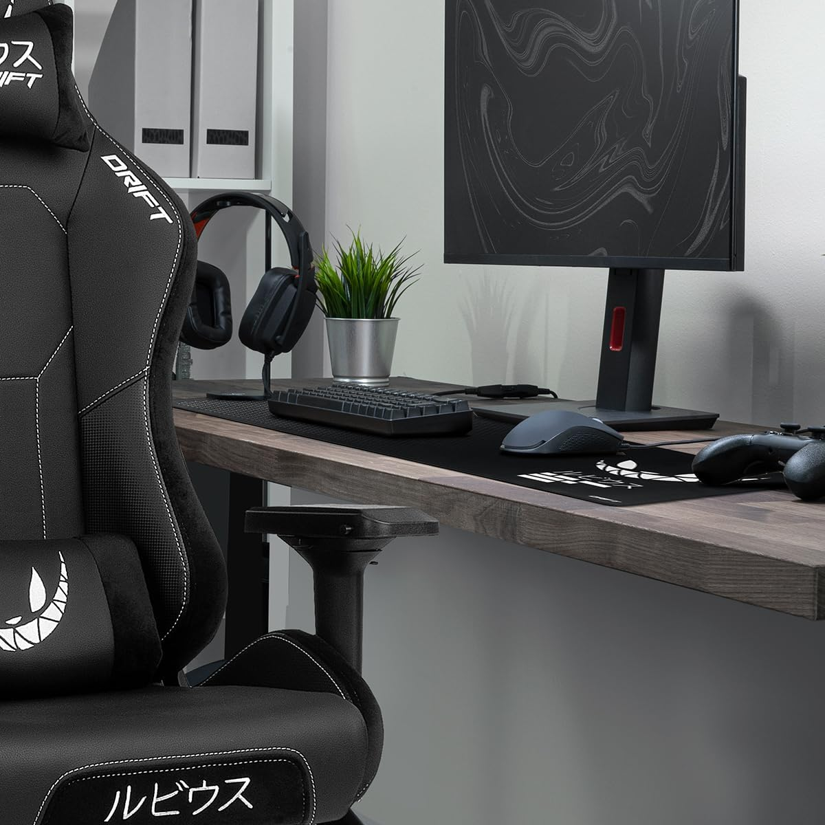 Una configuración de juego con una silla de juego negra, monitor, teclado y ratón, con una planta.