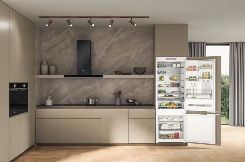 Wnętrze kuchni z lodówką, szafkami, okapem i innymi urządzeniami.