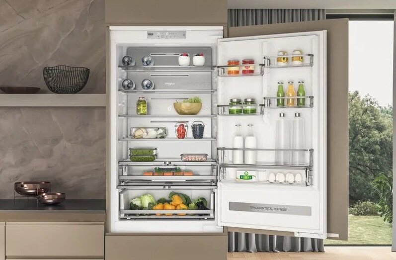 Otwarta lodówka wypełniona jedzeniem: owoce, warzywa i produkty pakowane.