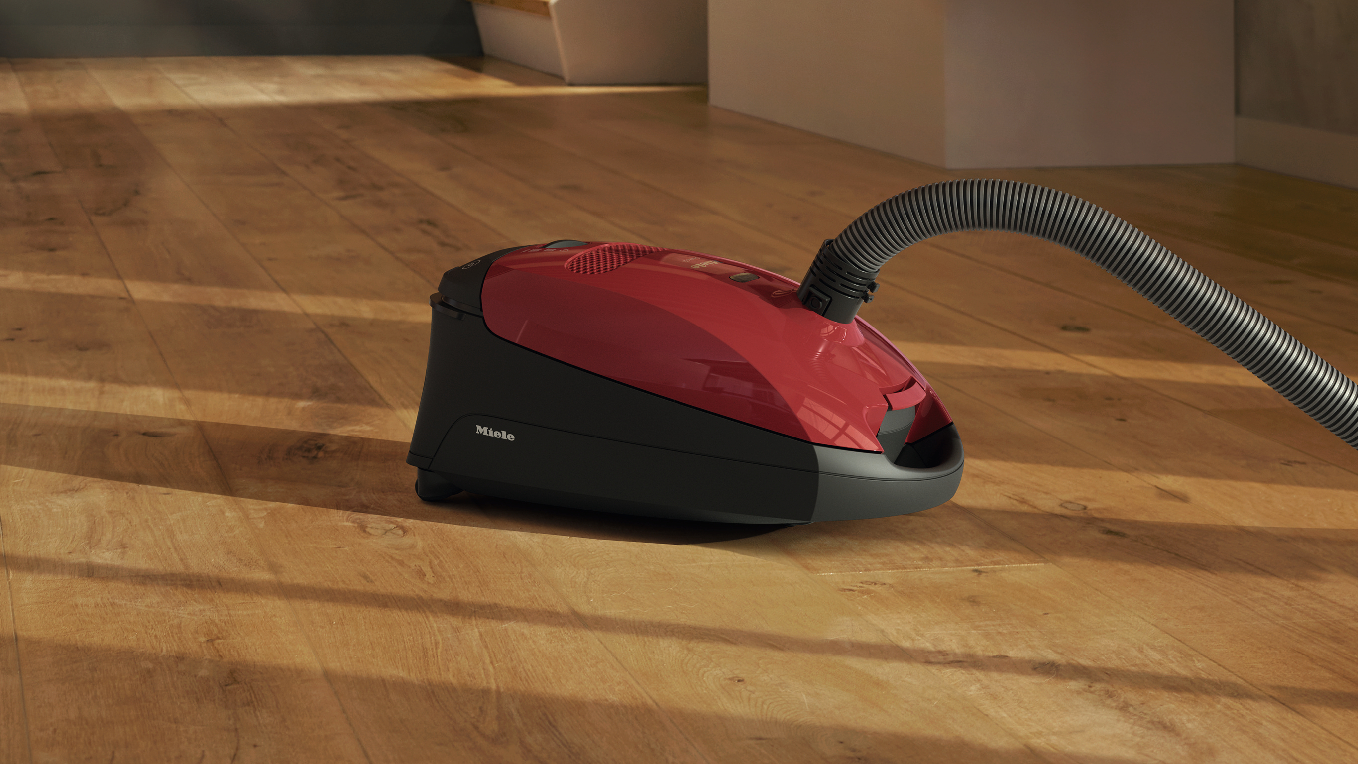 Ein roter und schwarzer Miele Staubsauger auf einem Holzboden.