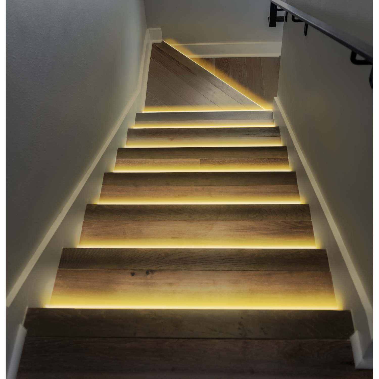 Wooden stairs with illuminated steps, ascending from a dark area.