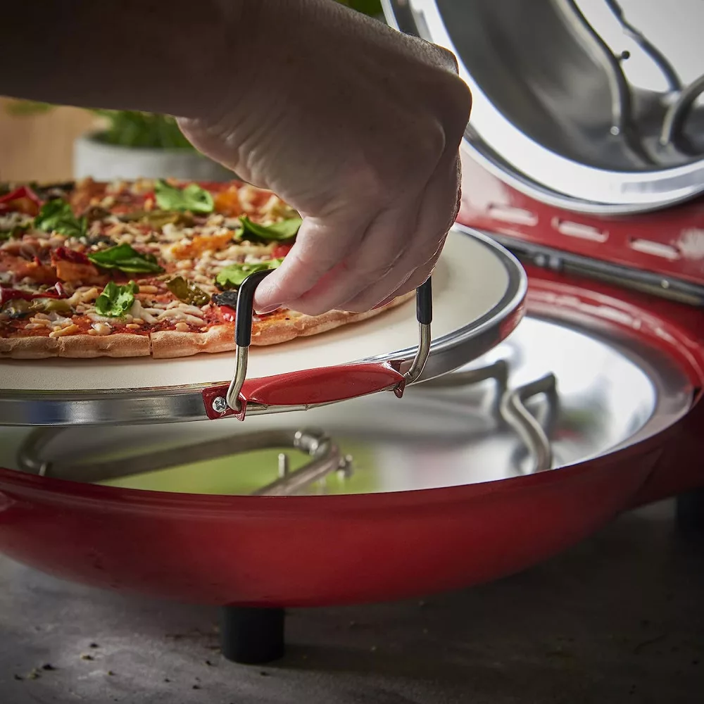 Személy pizzát helyez kőre egy piros pizzasütőben. A pizza tálcán van.