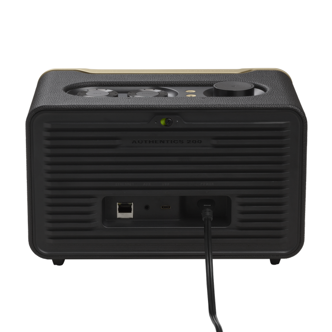 Un altavoz negro y dorado. La parte trasera del altavoz tiene puertos y un cable de alimentación conectado.