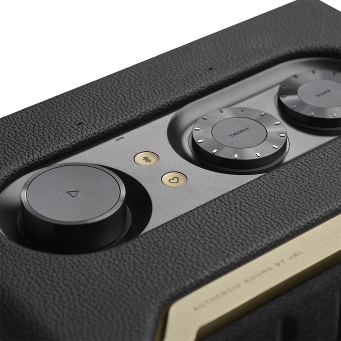 Primer plano del panel de control de un altavoz negro y dorado con perillas de ajuste de volumen y sonido.