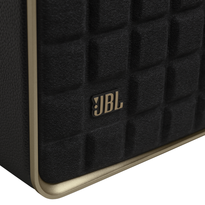 Primer plano de un altavoz negro con el logotipo de JBL, detalles dorados y diseño acolchado.