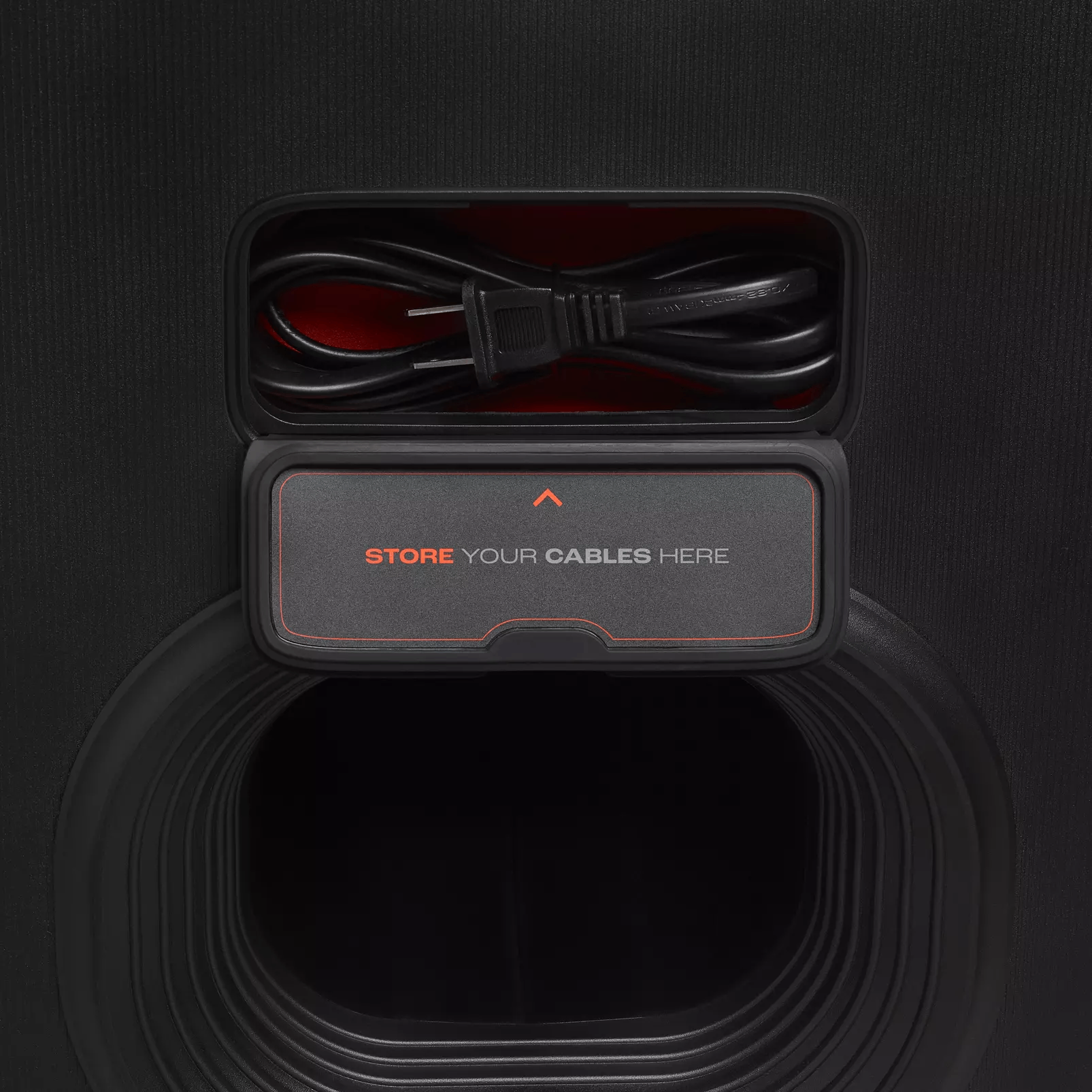 Un altavoz negro con un compartimento abierto con la etiqueta 'STORE YOUR CABLES HERE', mostrando cables.