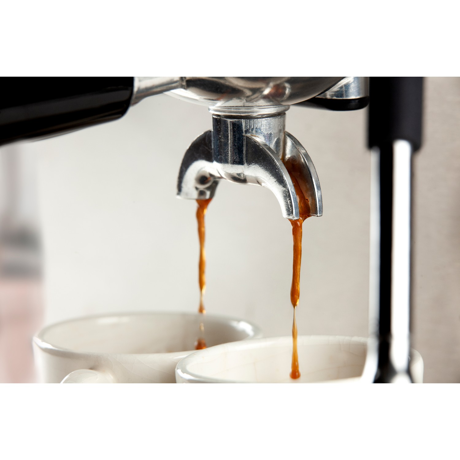 Close-up of espresso pouring into two white mugs. The machine's nozzle is visible.