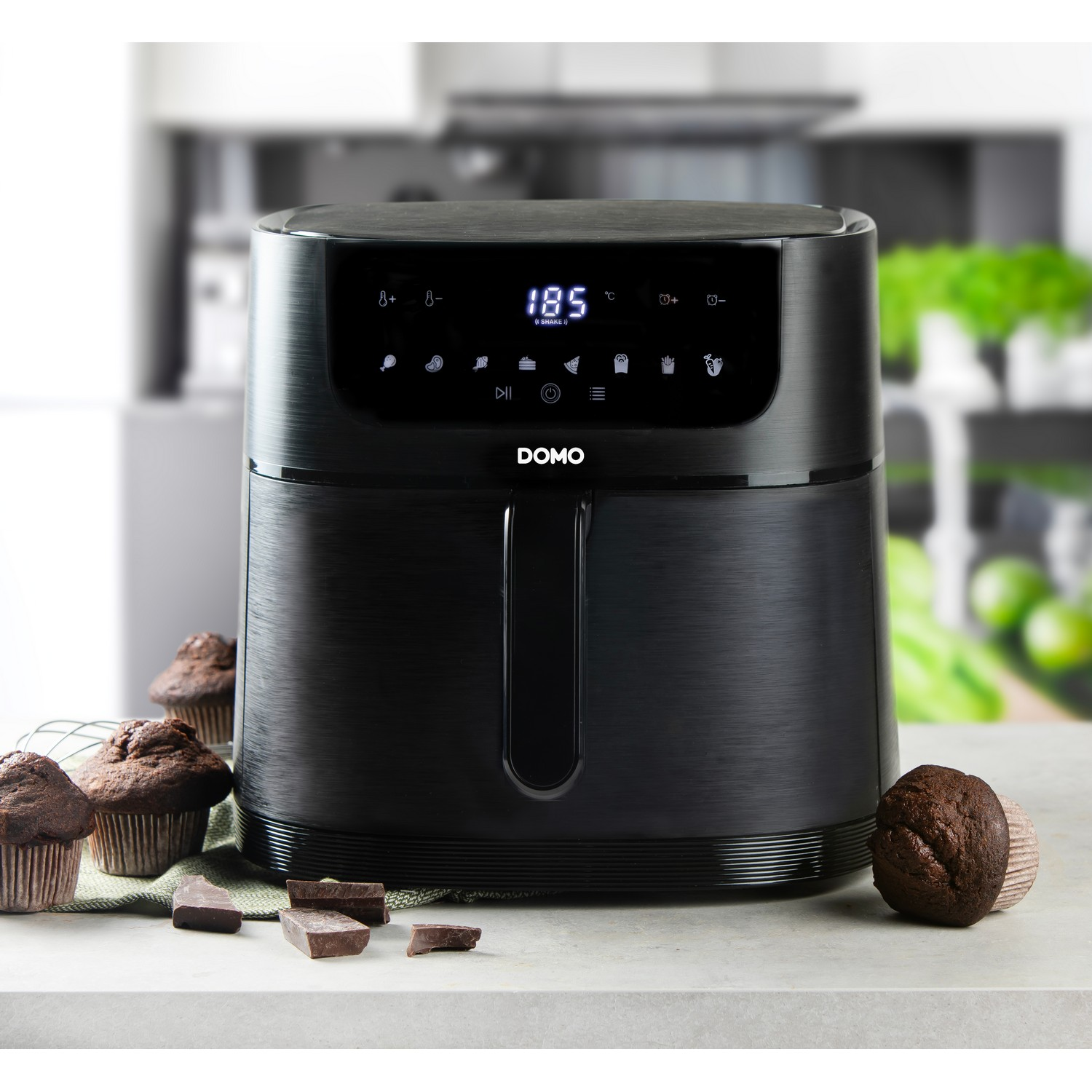 Une friteuse à air noire avec un écran numérique et des muffins au premier plan.