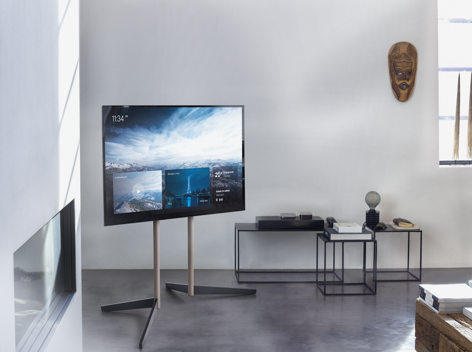 Ein modernes Wohnzimmer mit großem Fernseher, der eine malerische Aussicht zeigt. Eine Holzmaske hängt an der Wand. Tische und Dekor sind vorhanden.