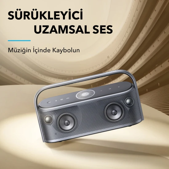 Gri bir Anker hoparlör, tutamağı, iki hoparlörü ve düğmeleri ile. Arka plan dalgalı bir desene sahip.