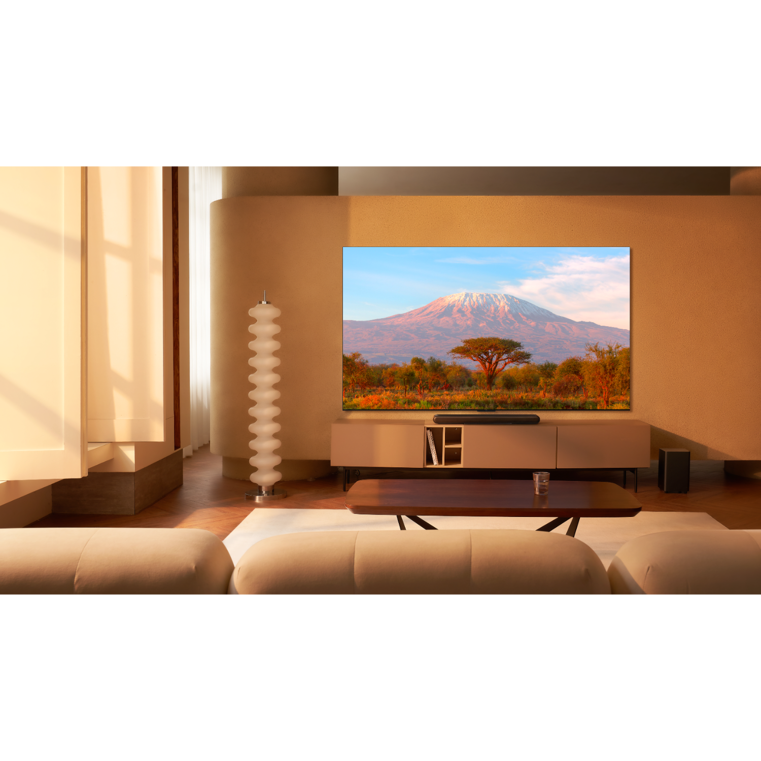 Woonkamer met grote tv met berglandschap. Beige muren en meubels.