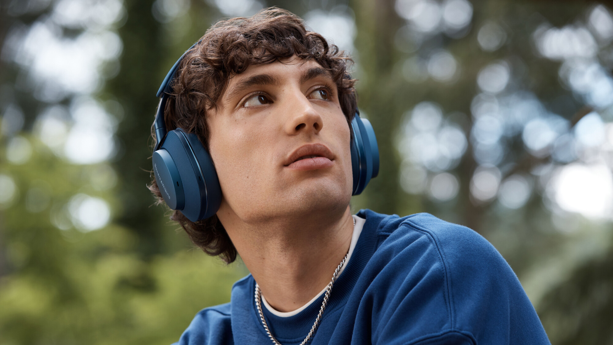 Ein Mann mit blauen Kopfhörern schaut nach oben. Er trägt einen blauen Pullover.
