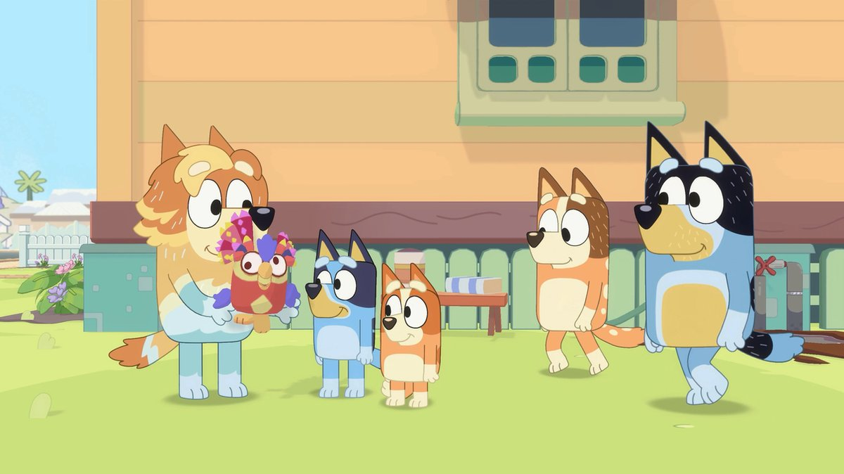 Les personnages de Bluey se tiennent sur l'herbe. La mère de Bluey tient un jouet en peluche.