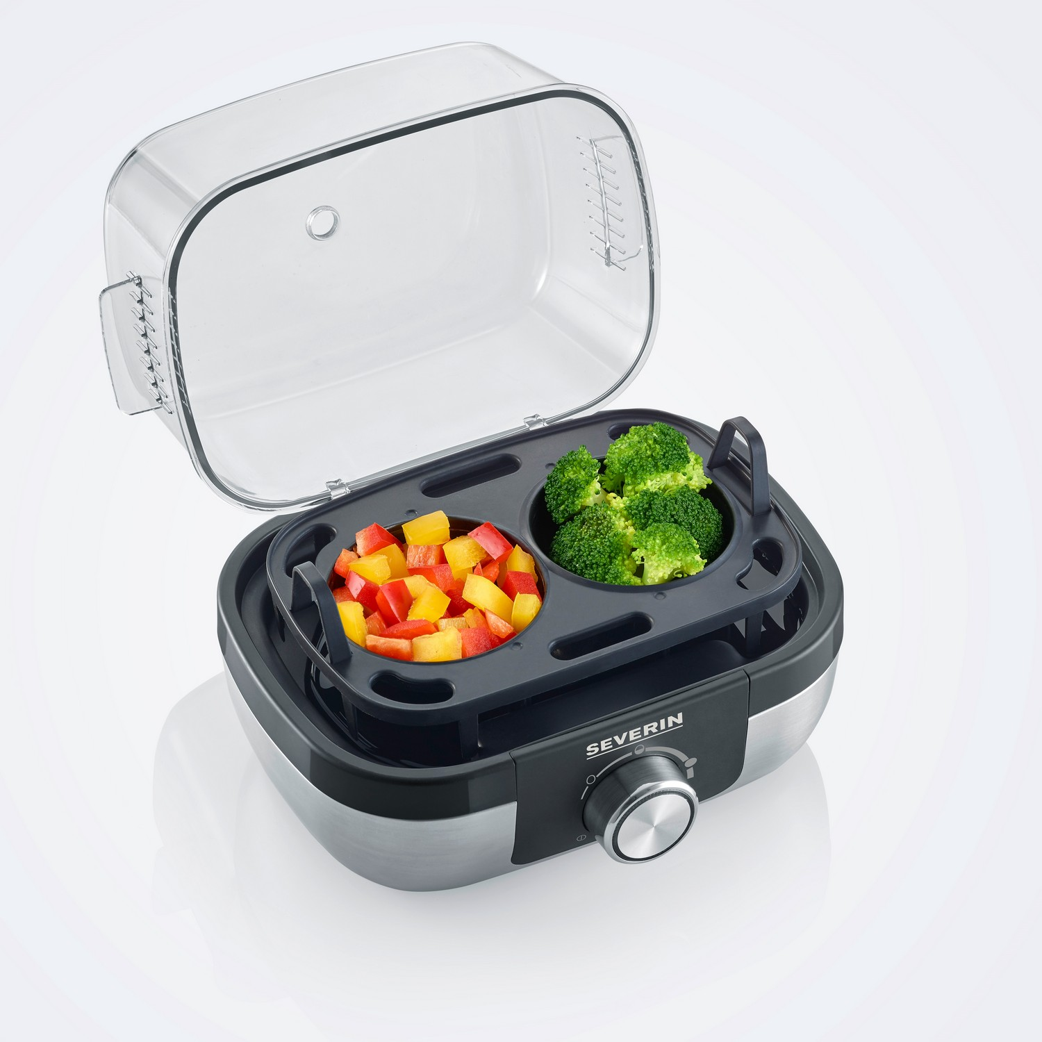 Un cuiseur d'œufs transparent avec des compartiments pour les légumes et les œufs. Le couvercle est ouvert, montrant le contenu.