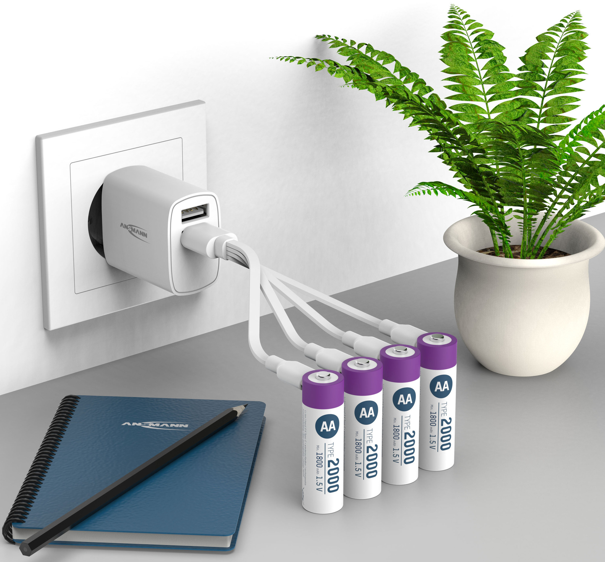 Chargeur blanc branché au mur, chargeant des piles AA. Cahier bleu et plante sur une surface grise.