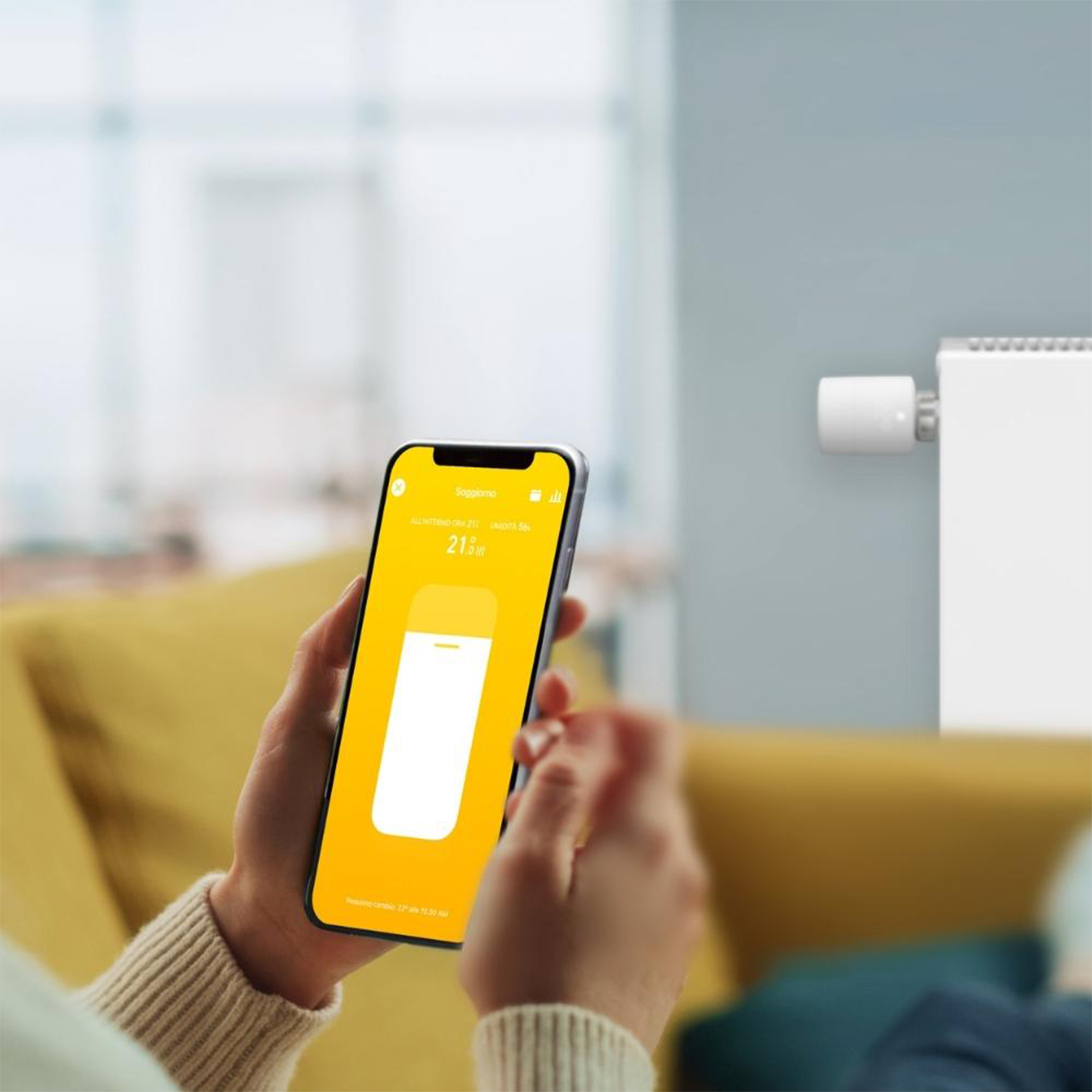 Persona che usa uno smartphone per controllare un termostato intelligente. Il telefono mostra un'interfaccia gialla.