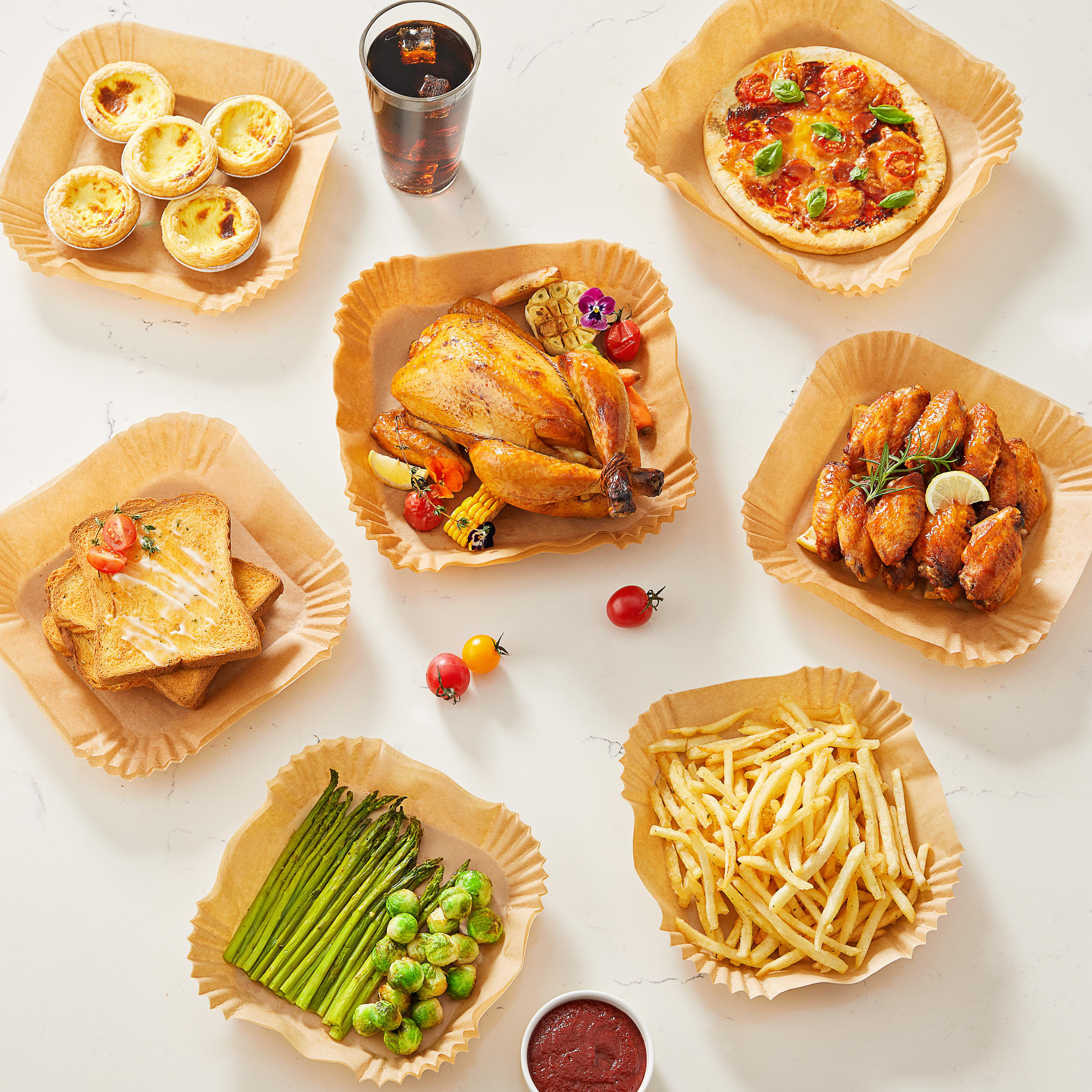 Eine Vielzahl von Lebensmitteln in Behältern aus braunem Papier: Pizza, Hähnchen, Pommes und Gebäck auf weißer Oberfläche.