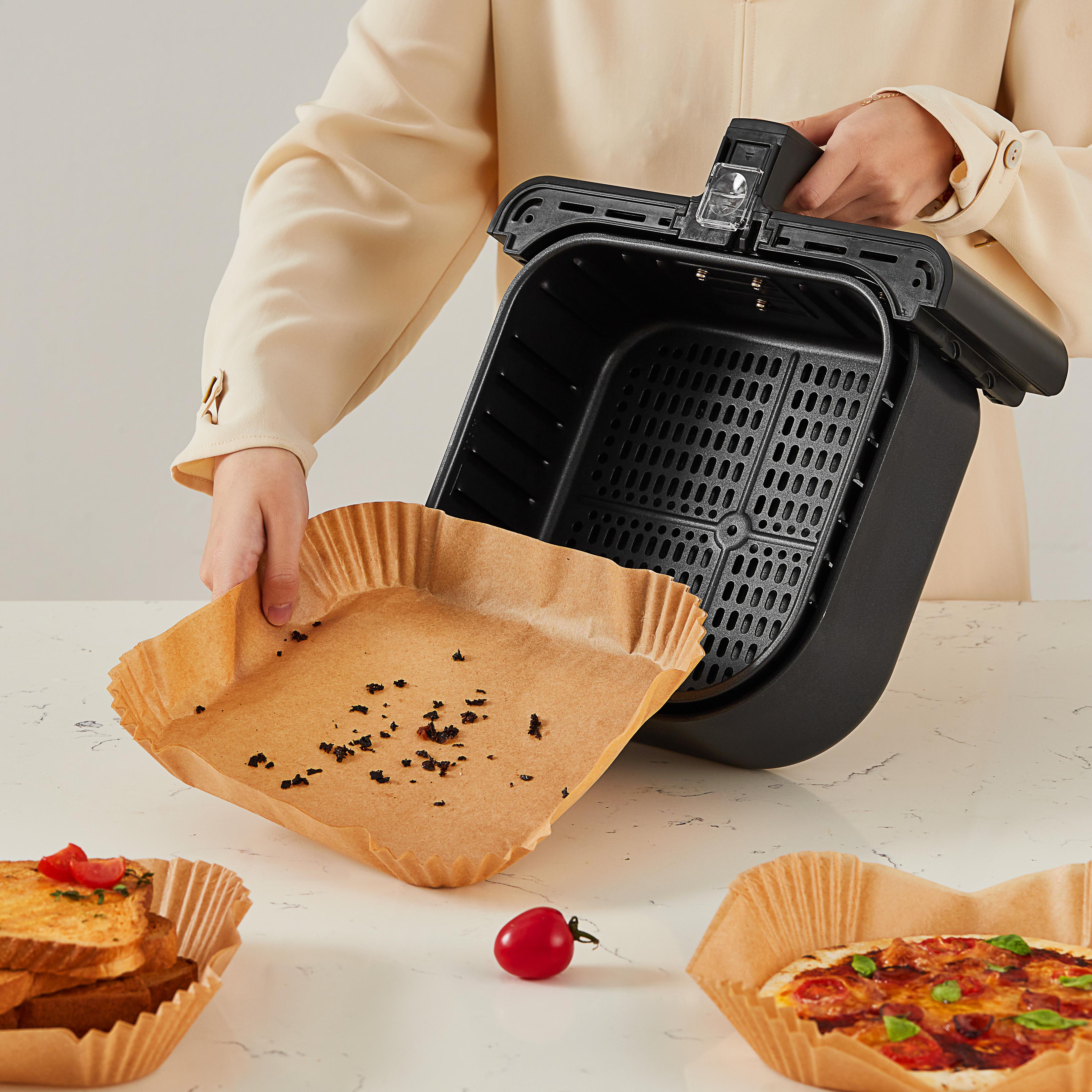Person hält eine Heißluftfritteuse-Korb und eine Papierauskleidung mit Essensresten. Anderes Essen in Tabletts.