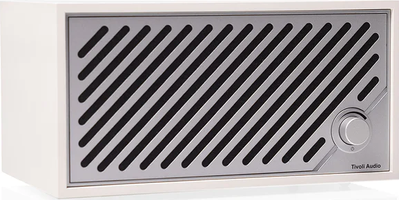 Un appareil audio blanc avec un panneau avant argenté comportant des ouvertures inclinées. Il possède un bouton de volume et le logo Tivoli Audio.