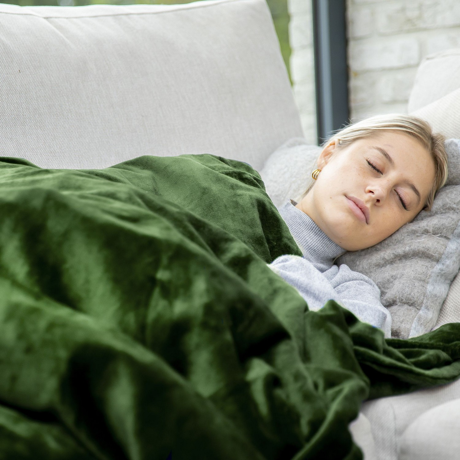 Une femme dormant sur un canapé, couverte d'une couverture verte, avec un oreiller gris sous la tête.