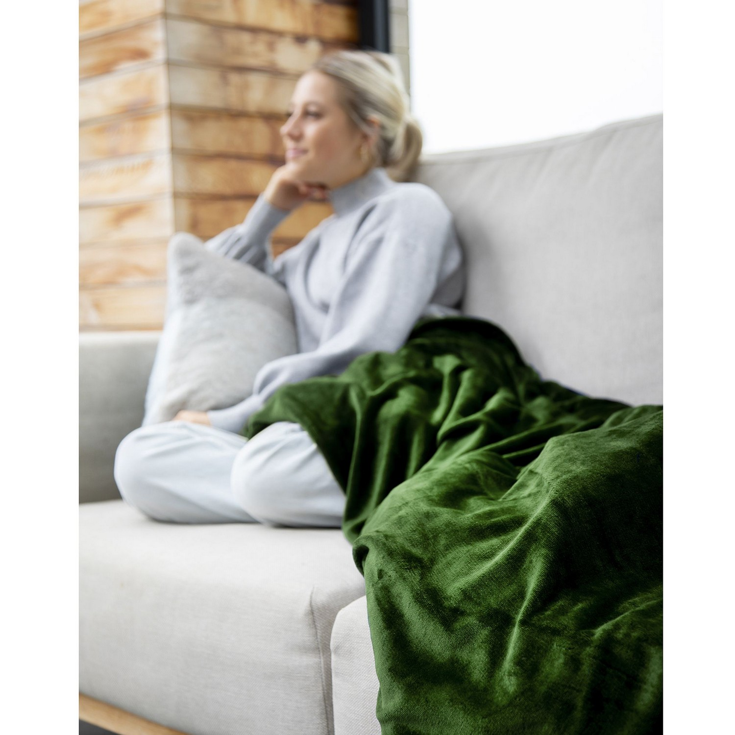 Femme sur un canapé avec une couverture verte, avec un oreiller, regardant ailleurs. Cadre douillet.