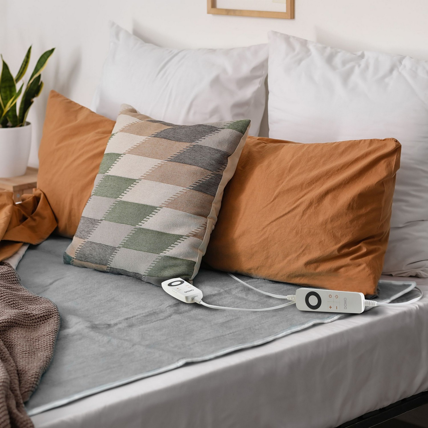 Lit avec oreillers et coussin chauffant. Oreillers beiges, oranges et à motifs. Draps blancs.