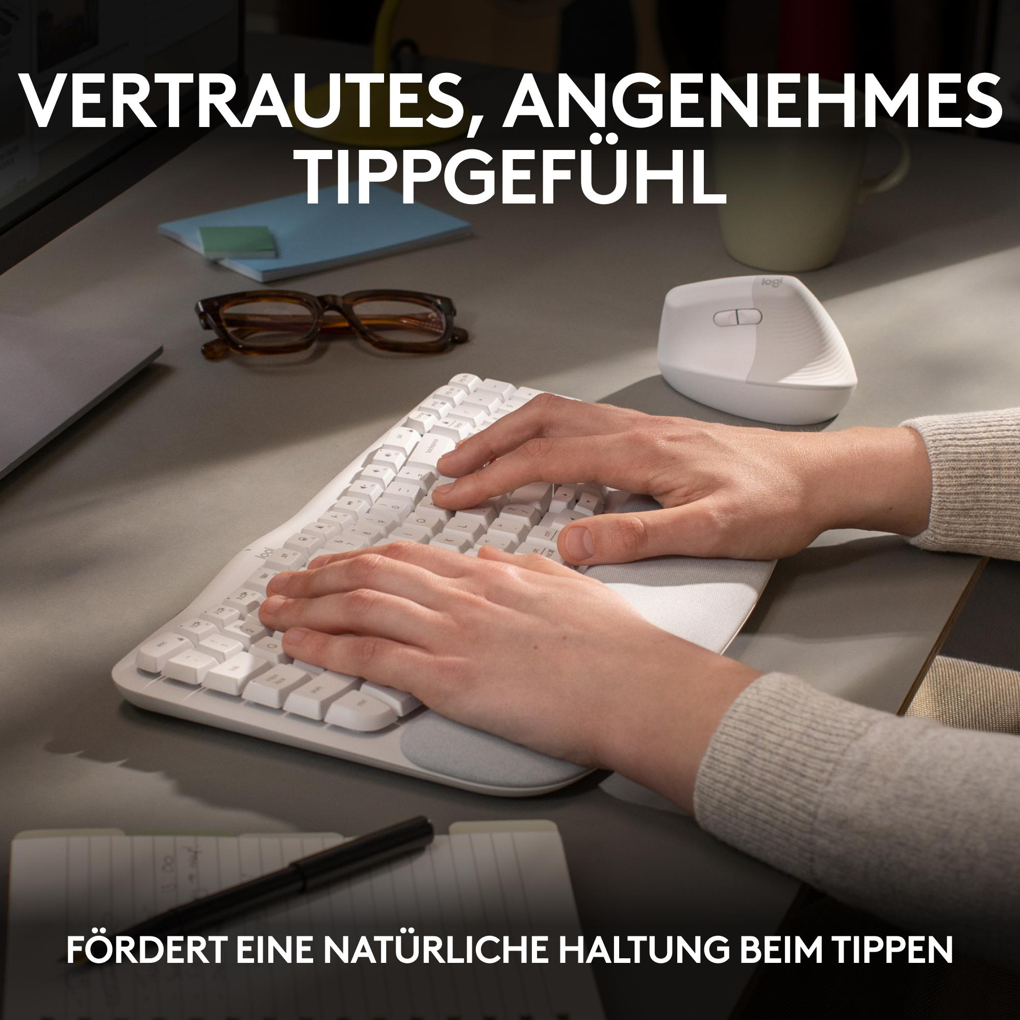 Hände einer Person tippen auf einer weißen ergonomischen Tastatur, daneben eine weiße Maus.