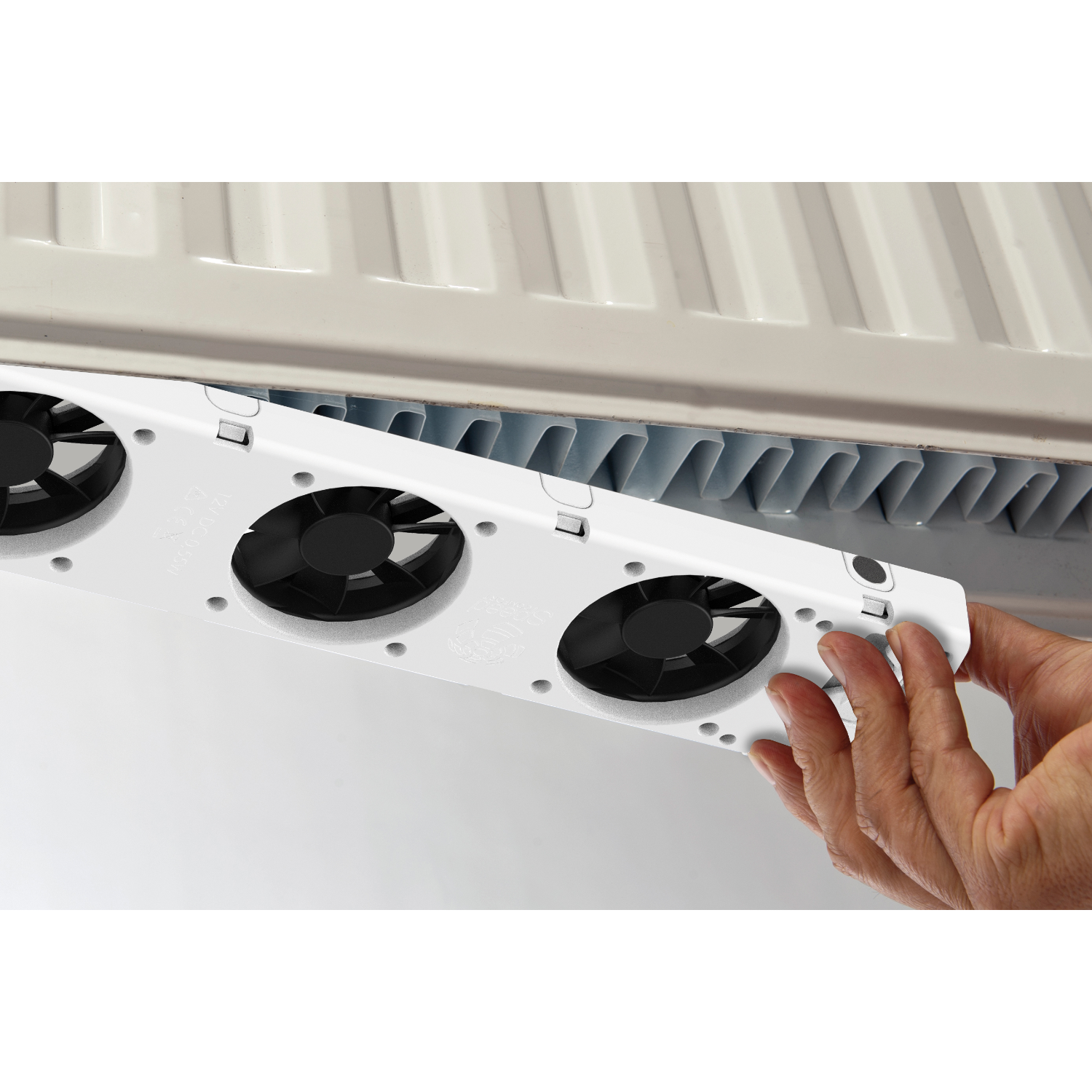 Hand holding a white fan unit under a white radiator. Black background.