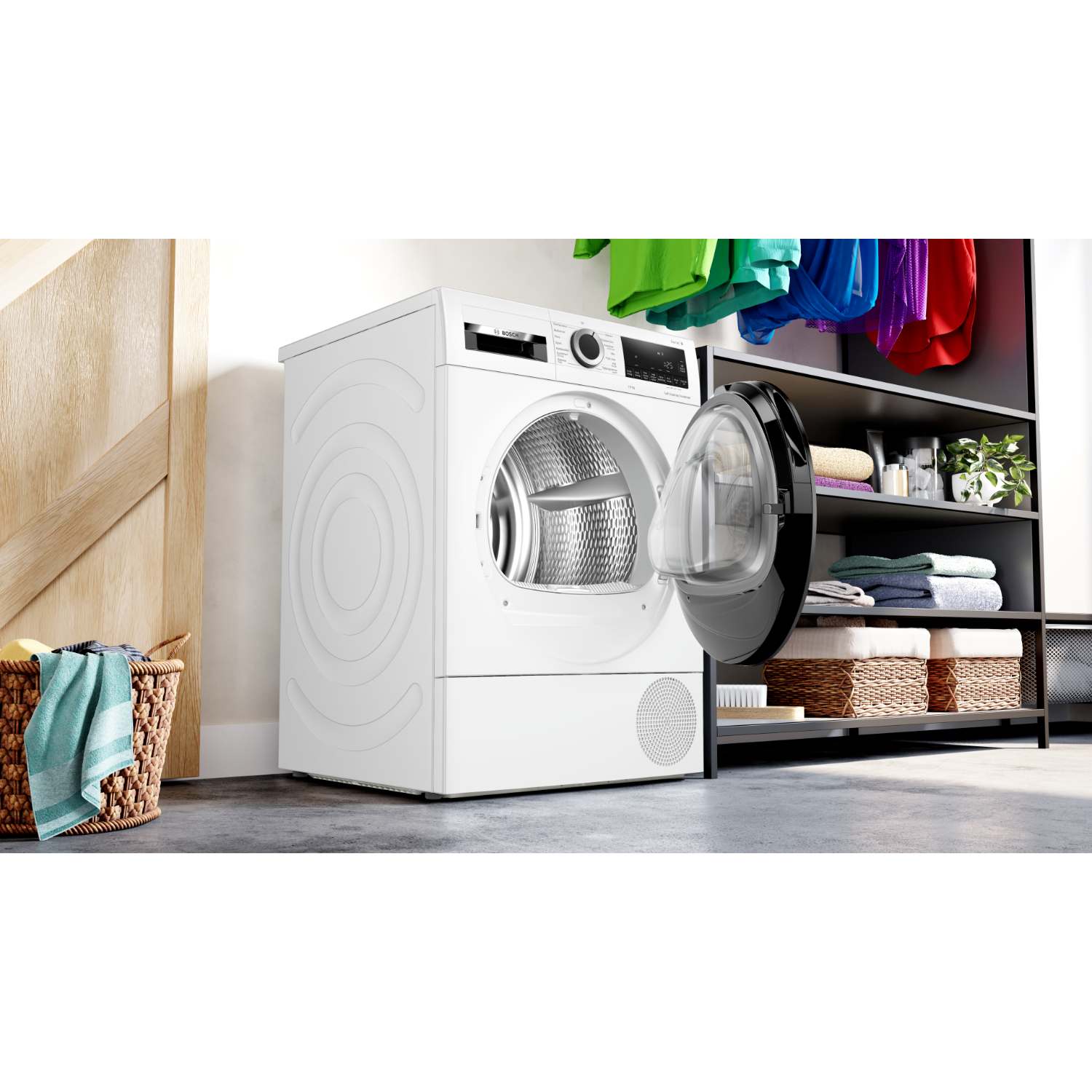 Een witte wasmachine met de deur open. Wasmand en hangende kleding in de scène.