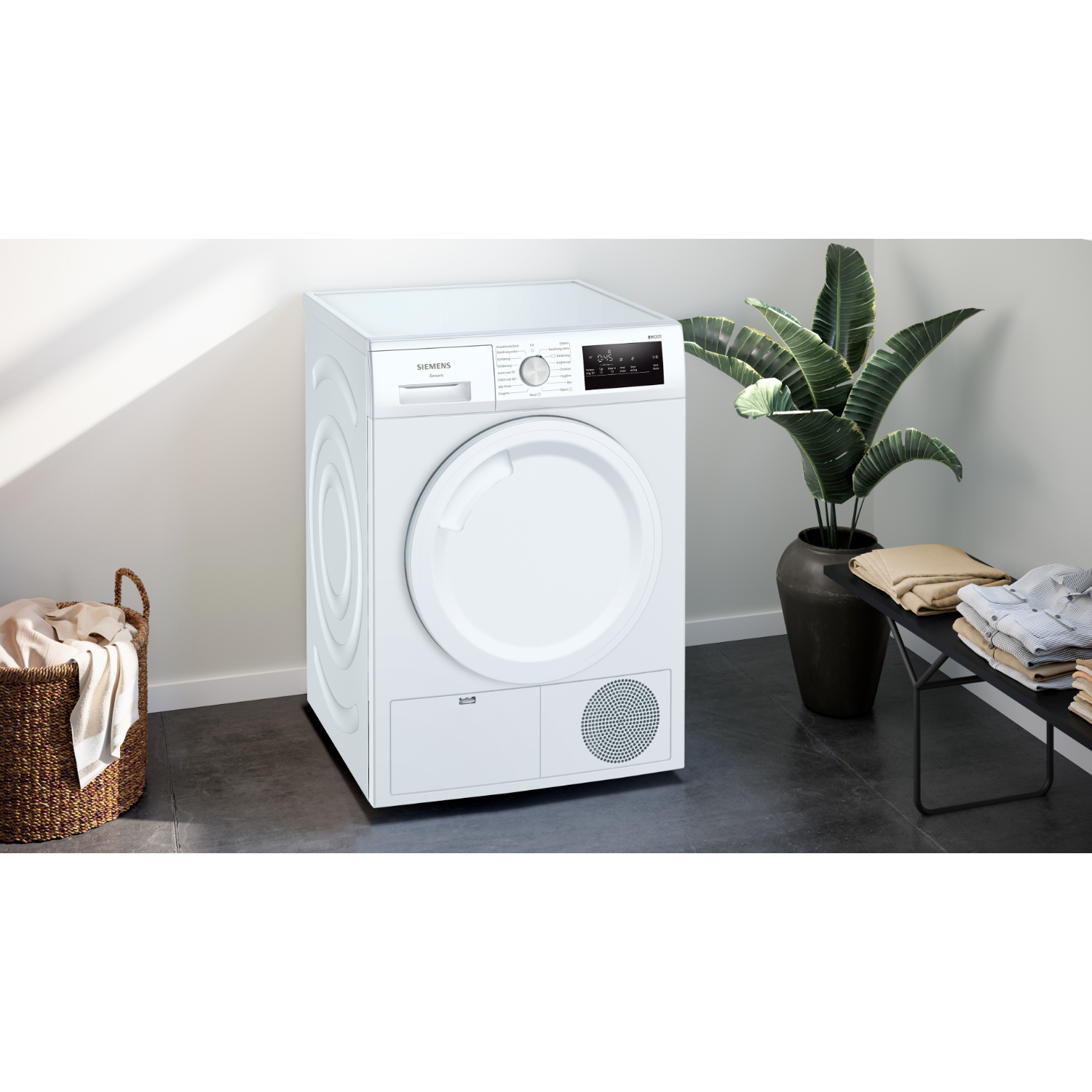 Een witte Siemens droger met een ronde deur, een wasmand en een plant in een pot.