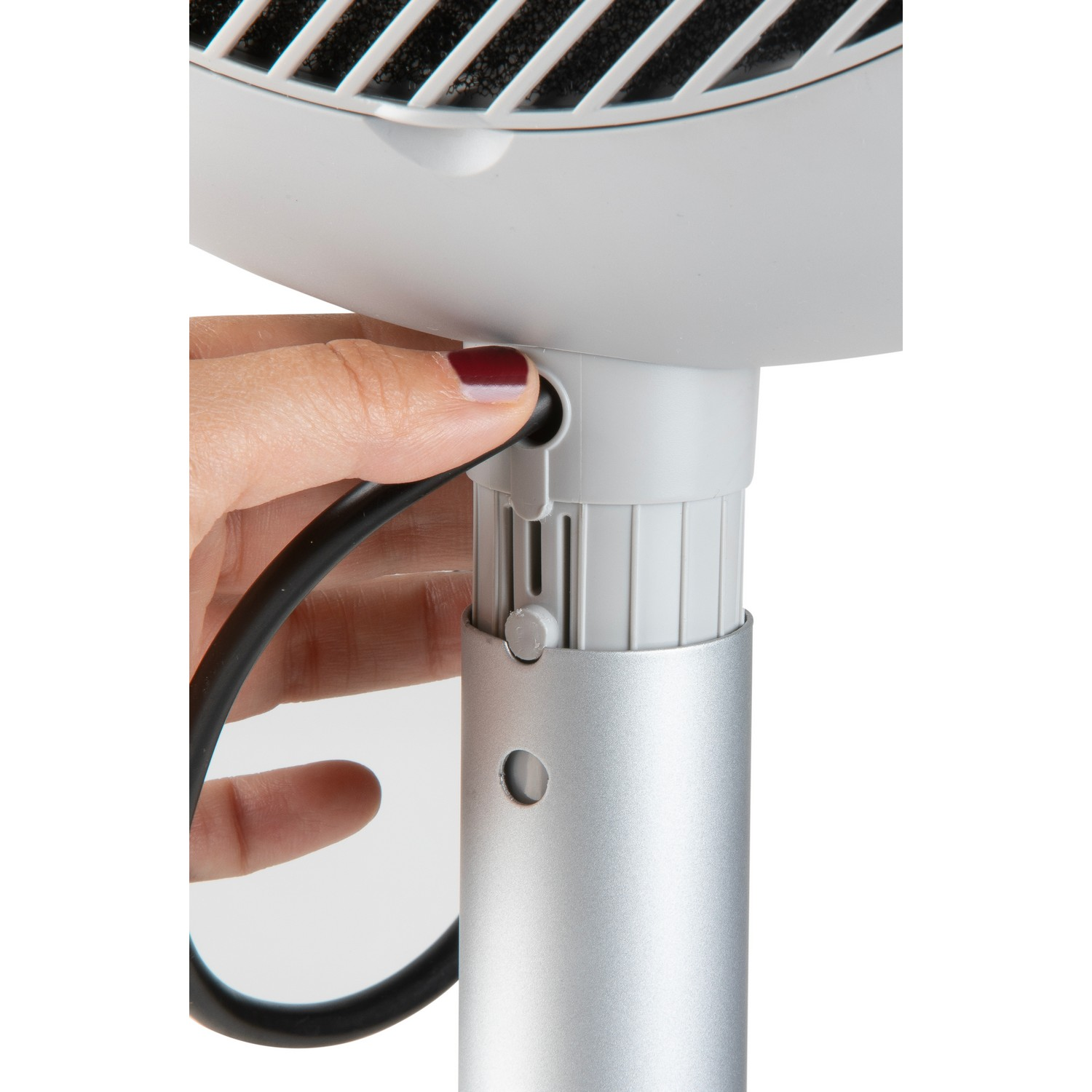 A hand is adjusting the height of a silver fan's stand.