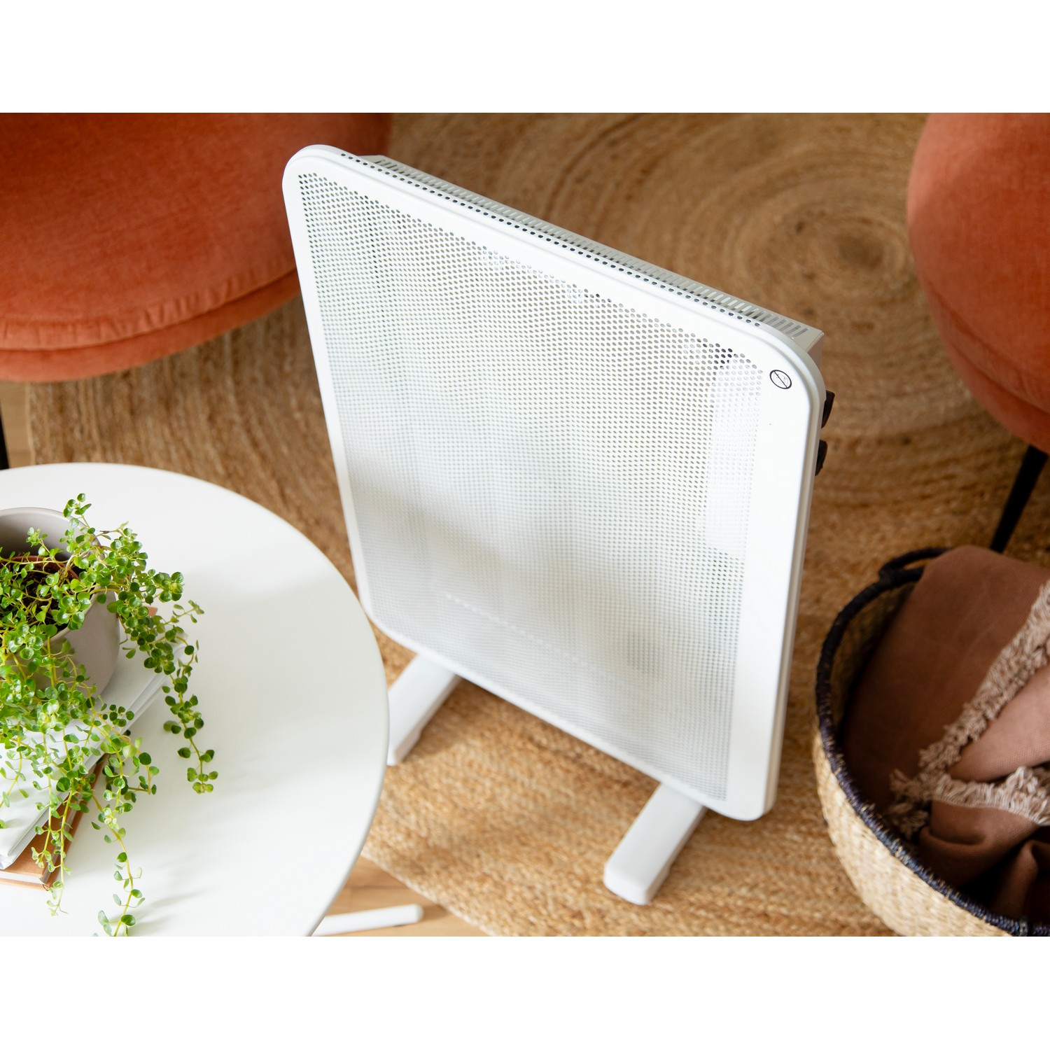 White electric heater on a rug. A table and chairs are nearby, with a plant and blanket.