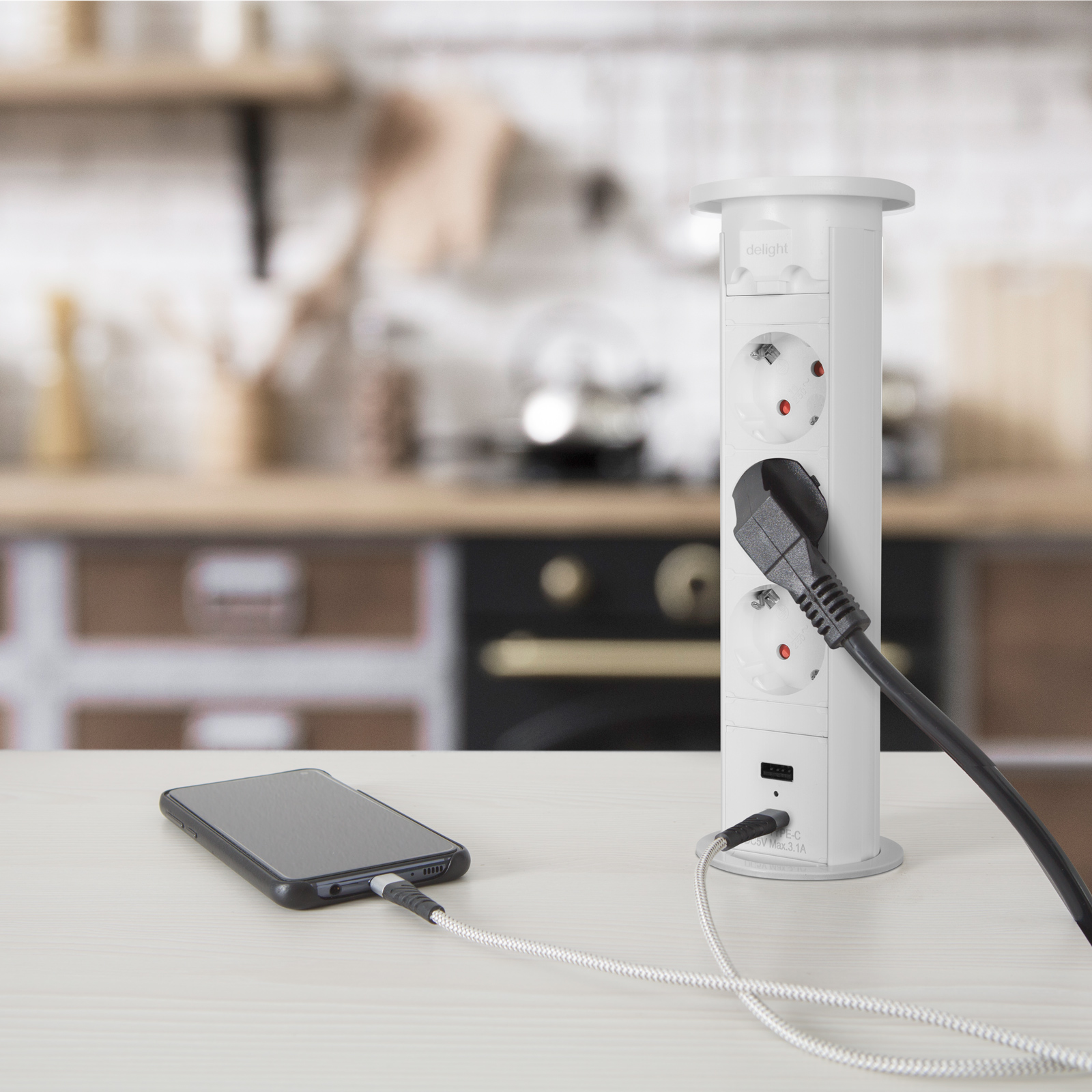 Fehér konnektor USB portokkal egy fehér asztalon. Egy telefon töltődik a közelben.