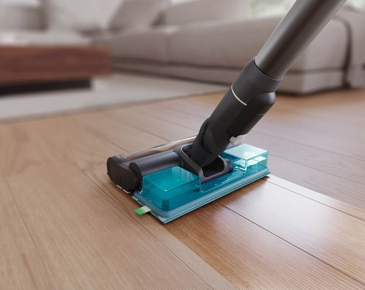 Głowica odkurzacza czyszcząca drewnianą podłogę. Niewyraźne tło, biała sofa.