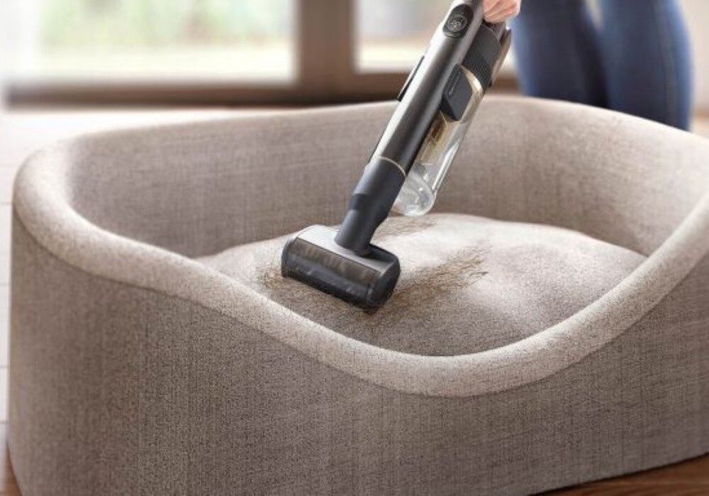 Ręczny odkurzacz służy do czyszczenia legowiska dla psa. Legowisko jest szare.