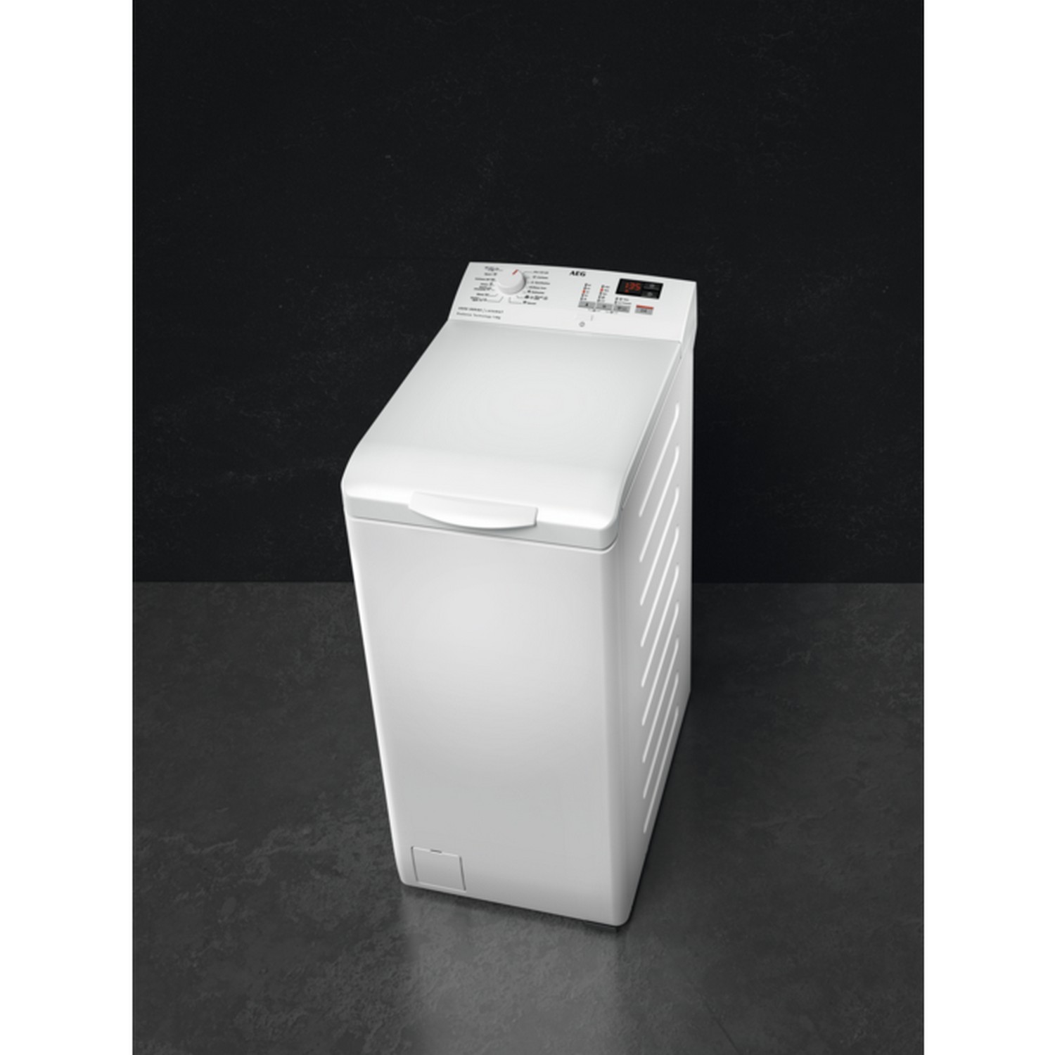 Een witte AEG wasmachine staat op een donkergrijze vloer tegen een zwarte achtergrond. De machine heeft een bedieningspaneel aan de bovenkant.
