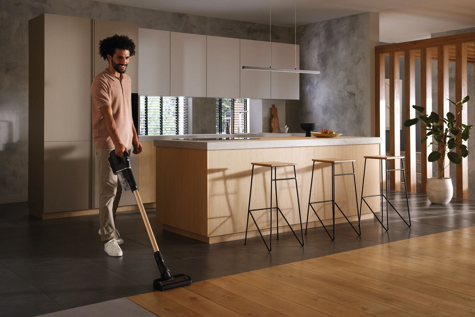 Un homme passant l'aspirateur sur un sol en bois dans une cuisine moderne. Un aspirateur sans fil est utilisé.