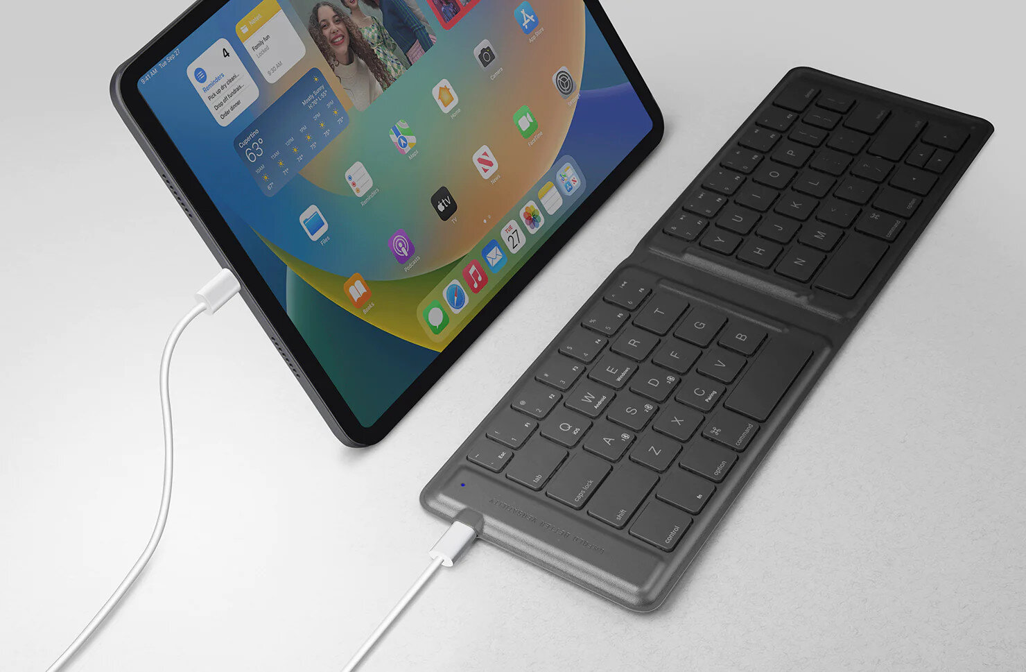 iPad Pro z dołączoną klawiaturą Apple. iPad wyświetla ekran główny. Podłączony jest kabel do ładowania.