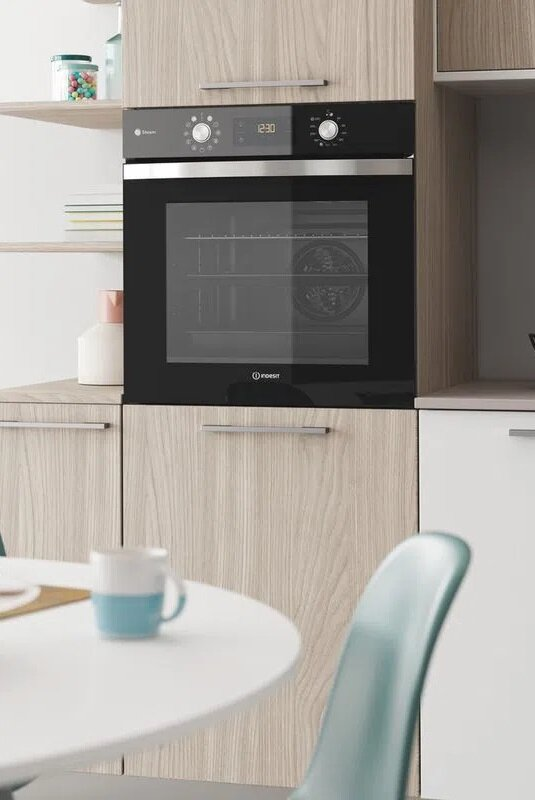 Piekarnik do zabudowy, czarne drzwi, drewniane szafki. Biały stół i turkusowe krzesło na pierwszym planie.