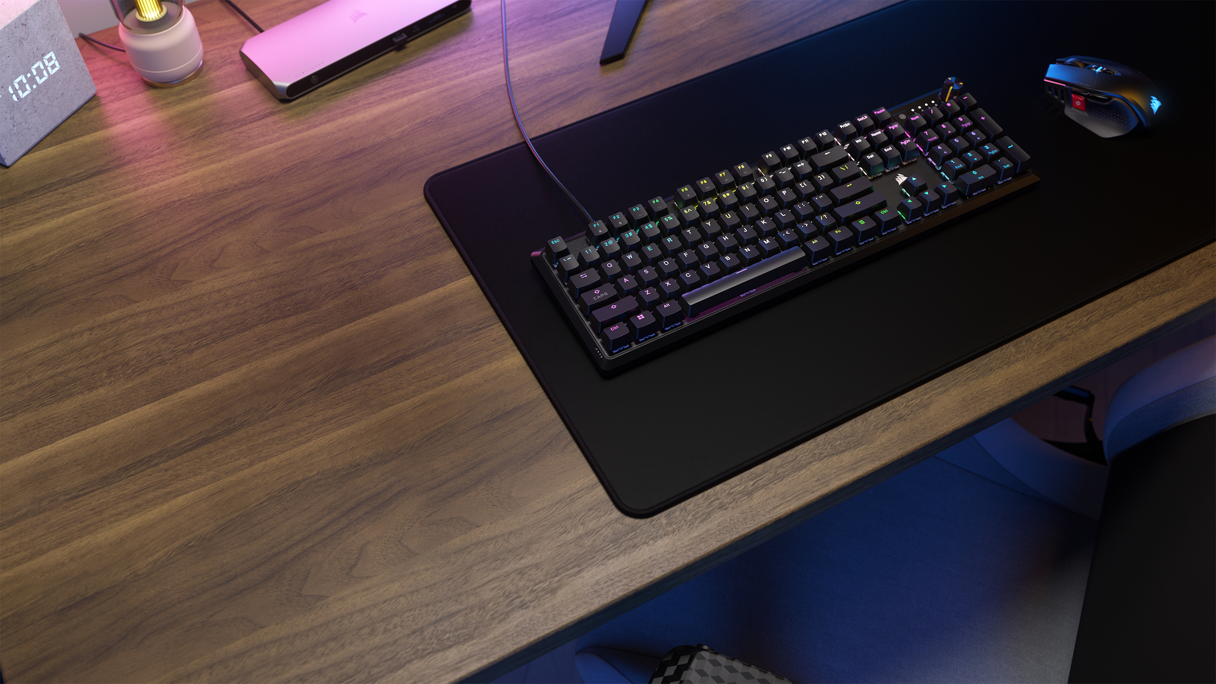Ein Holzschreibtisch mit Tastatur, Maus und digitaler Uhr. Die Tastatur hat Regenbogenlichter.