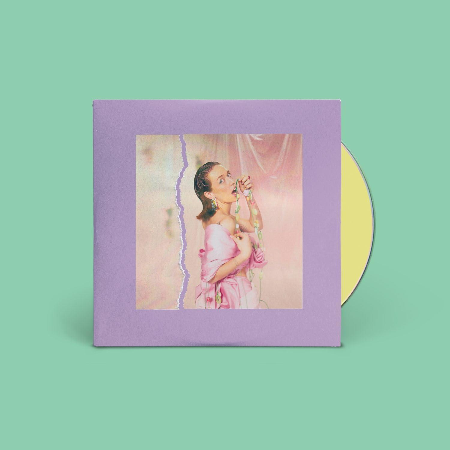 Ein CD-Albumcover mit einer Frau in Rosa, einem zerrissenen Papiereffekt und einer gelben CD.