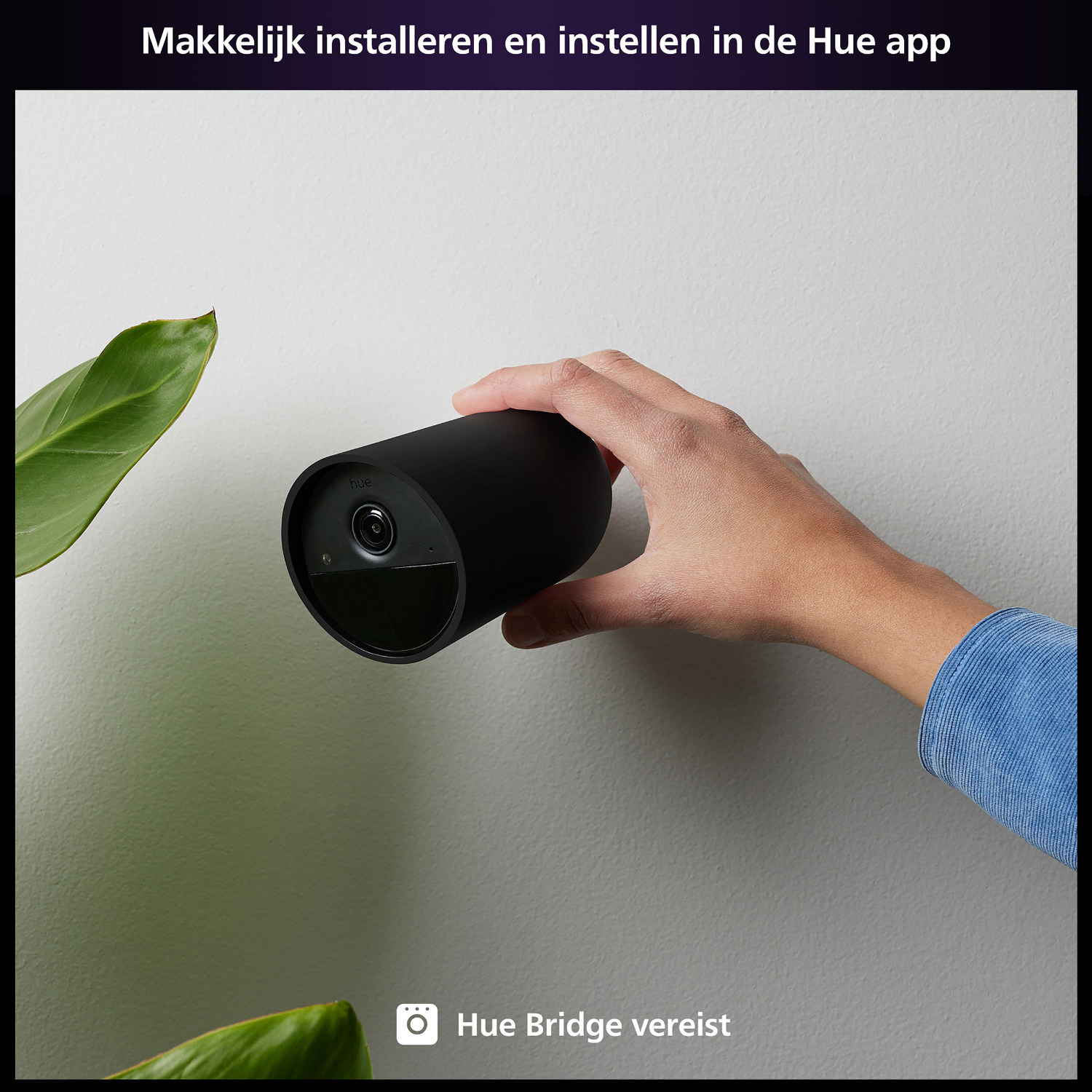 A hand holds a black cylindrical device. Plant in the background. Text: Easy install and set up in the Hue app.