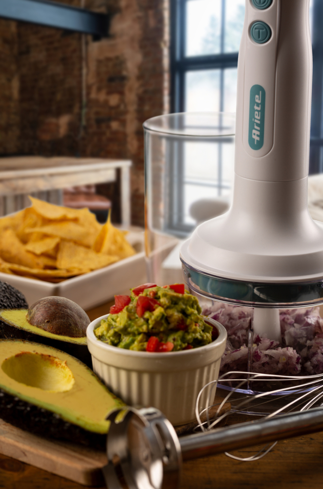 Guacamole, avokádók és egy botmixer egy fa deszkán egy konyhai jelenetben.