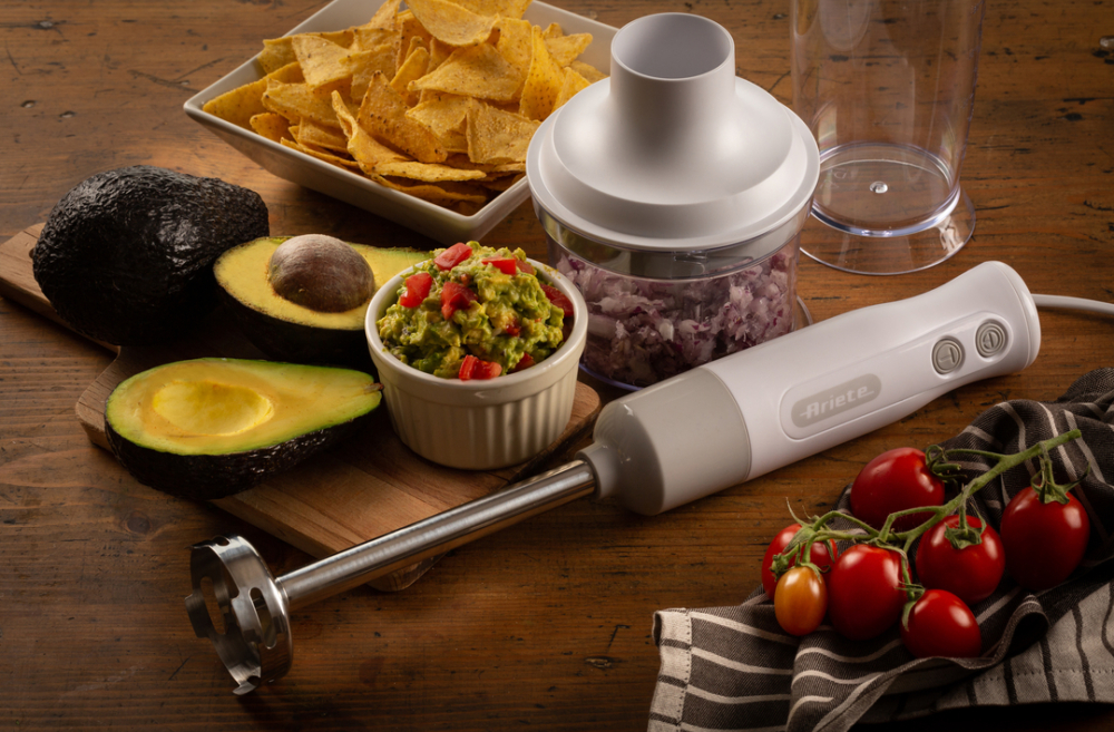 Guacamole hozzávalók és egy botmixer egy fa felületen.