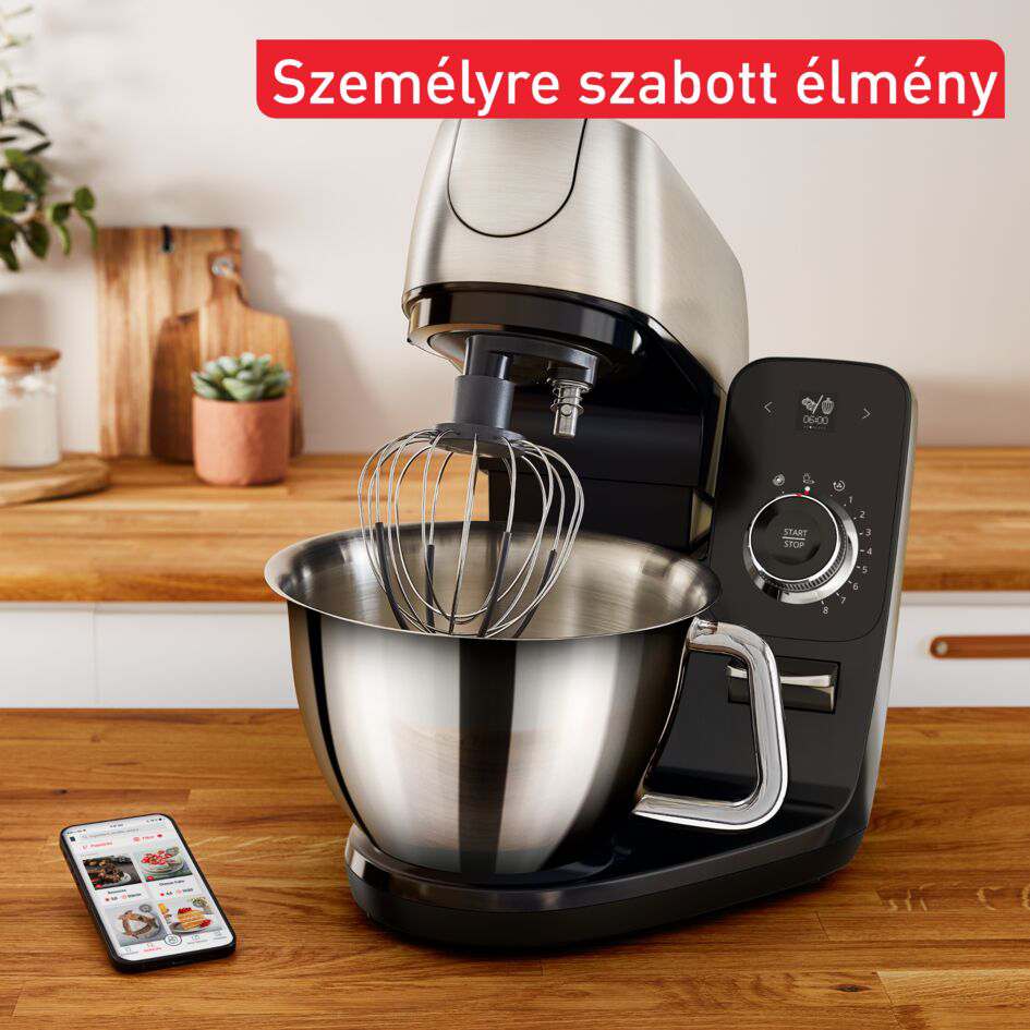 Konyhai készülék tálkával és okostelefonnal, amely egy receptalkalmazást jelenít meg.