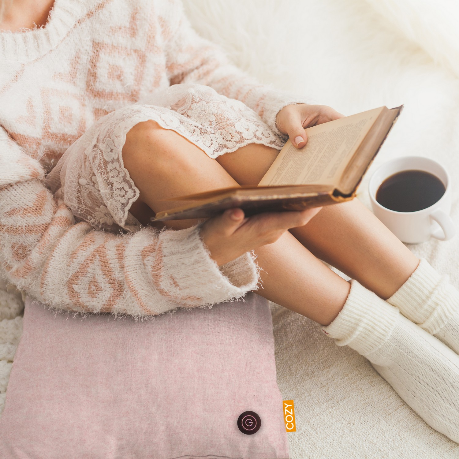 Une personne lit un livre sur un coussin rose, avec une tasse de café.